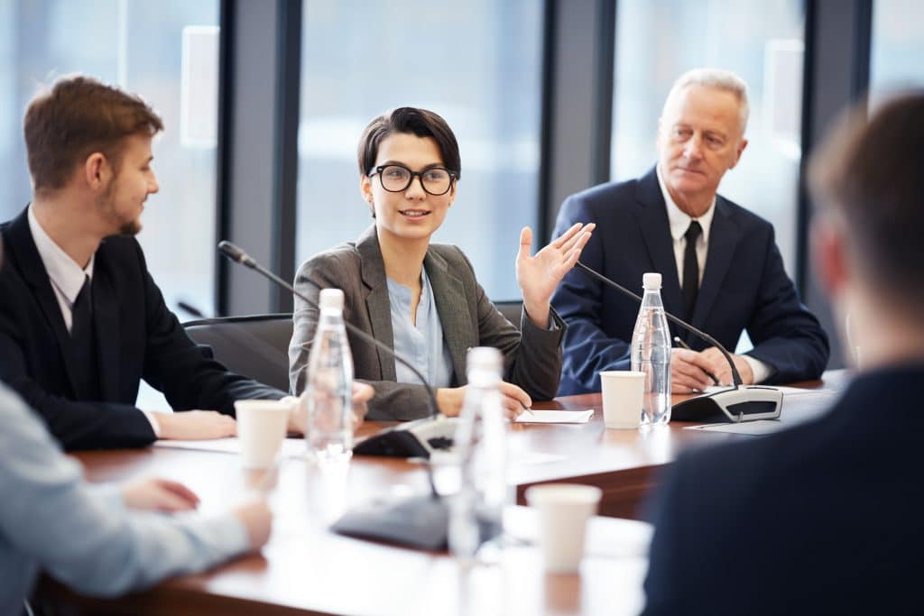 Portrait of young businesswoman speaking to microphone during group discussion in conference room, copy space